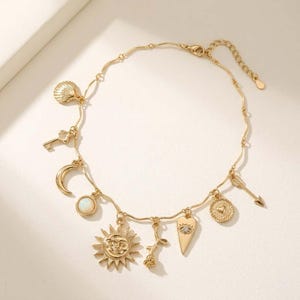 May include: Gold-colored charm bracelet featuring various celestial and symbolic charms. Charms include a seashell, key, crescent moon, sun, rose, heart, arrow, and a coin with a heart. The bracelet has an adjustable chain.