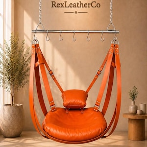 Puede incluir: Un asiento colgante de cuero naranja suspendido por correas de cuero gruesas y cadenas metálicas de una barra horizontal con seis ganchos. El asiento incluye un cojín de cuero naranja a juego y presenta el texto RexLeatherCo encima.