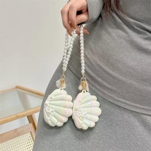 May include: Two iridescent white seashell-shaped accessories with pearl beaded straps. The accessories have gold-coloured accents and are held by a person. The shells have a pearlescent sheen and are detailed with radial lines.