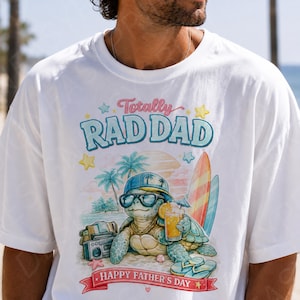 May include: A white t-shirt featuring a graphic of a turtle wearing sunglasses and a hat, holding a drink on a beach. The text reads Totally RAD DAD and HAPPY FATHER'S DAY. The design includes palm trees, surfboards, and a boombox.