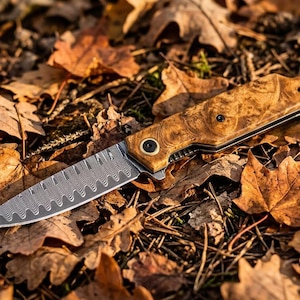 May include: A folding pocket knife featuring a silver-toned blade with a distinct wavy, layered pattern and a handle crafted from polished, light brown burl wood with visible dark grain swirls and two black circular screw fasteners.