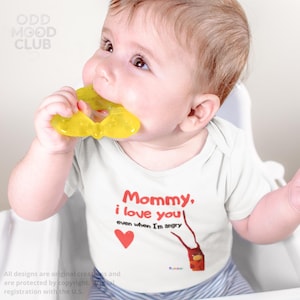 May include: A baby wearing a white onesie with the text "Mommy, I love you! even when I'm angry" in red. The baby is holding a yellow teether in their mouth. A red heart and a small illustration are also on the onesie.