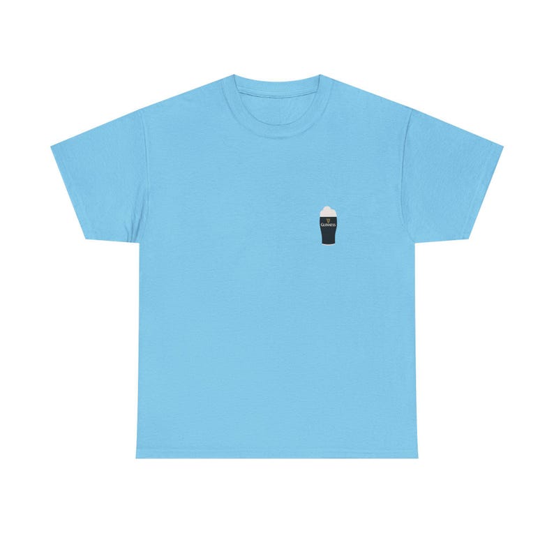 May include: Light blue t-shirt with a small graphic of a pint of stout on the left chest. The pint glass is black with a white foamy head and the word "Guinness" in white. The shirt is made of a soft material.
