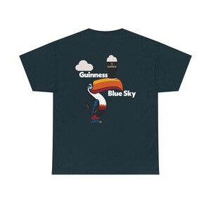 May include: Dark teal t-shirt featuring a toucan with a large orange and yellow beak. The toucan is positioned below the words "Guinness" and "Blue Sky" with a Guinness pint graphic and a cloud graphic.