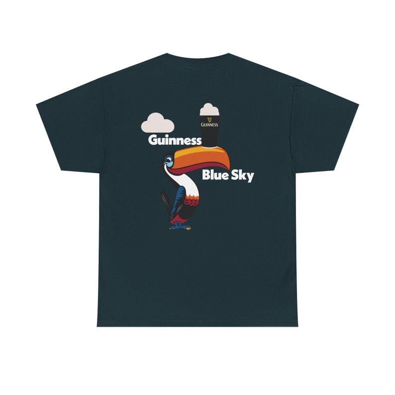 May include: Dark teal t-shirt featuring a toucan with a large orange and yellow beak. The toucan is positioned below the words "Guinness" and "Blue Sky" with a Guinness pint graphic and a cloud graphic.