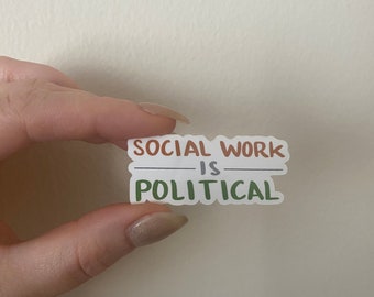 May include: A rectangular sticker with the text "SOCIAL WORK IS POLITICAL" in brown, green, and white. The sticker is held between fingers against a neutral background. The text is in a sans-serif font.