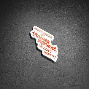 May include: A white sticker with red text that reads "IF YOUR INTERVENTION ISN'T trauma informed, WE DON'T WANT IT!" The sticker is in a stylized shape and is placed on a dark gray surface.