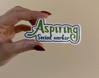 May include: A white sticker with the words "Aspiring Social Worker" in green and blue lettering. The sticker is held by a hand with red nail polish.
