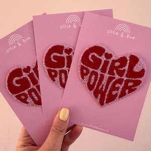 May include: Three pink cards featuring a red glitter heart with the words "Girl Power". Each card has a rainbow logo and the text "Ollie & Eve". The website address www.ollieandeve.co.uk is printed on the bottom right corner of the cards.