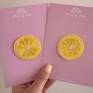 May include: Two yellow lemon slice patches with white borders are displayed on pink cards. The cards have the text "ollie & Eve" and a rainbow logo at the top. The website address www.ollieandeve.co.uk is at the bottom.