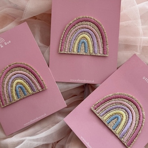 May include: Pastel rainbow embroidered patches with gold glitter edging, displayed on pink cards. The rainbow design features pink, purple, yellow, and blue. Each card is branded with "Ollie & Eve" and a website address.