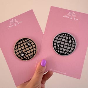 May include: Two circular embroidered patches with a disco ball design and star details. One is gold, the other silver, both with black borders. They are presented on pink cards with "Ollie & Eve" and a website address.