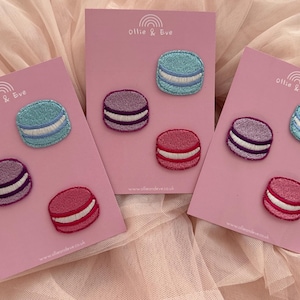 May include: Embroidered macaron patches in pink, purple, and blue with white filling, presented on pink cards. The cards feature the text "Ollie & Eve" and a website address.