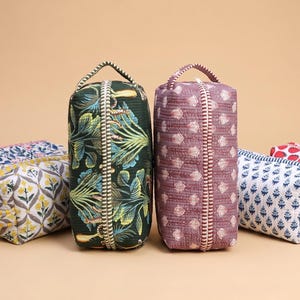 May include: Six rectangular quilted pouches with top handles and zippered closures. The pouches feature various patterns including blue floral, yellow and grey floral, dark green botanical, mauve geometric, blue geometric, and red strawberry prints.