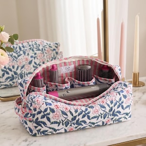 May include: A quilted fabric storage bag featuring a blue and pink floral print on a white background. The interior is lined with a red and white striped fabric and contains multiple compartments holding a grey hair dryer and various styling attachments.