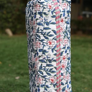 K&ouml;nnte beinhalten: Eine rechteckige, gesteppte Stofftasche mit wei&szlig;em Grund und einem sich wiederholenden Blumenmuster in Blau-, Gr&uuml;n- und Rosat&ouml;nen. Die Tasche verf&uuml;gt &uuml;ber einen Tragegriff und einen vertikalen Rei&szlig;verschluss mit rosa-wei&szlig; gestreifter Einfassung.