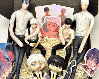 Puede incluir: Una colección de dos muñecos de tela altos con cabello negro y blanco, dos figuras sentadas más pequeñas y dos figuras estilo chibi, todos con camisas blancas y pantalones oscuros. Se incluyen varias tarjetas ilustradas y pegatinas con personajes.
