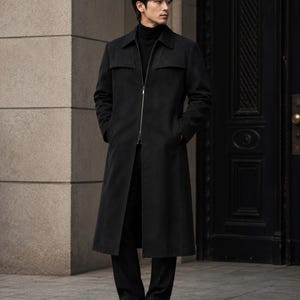 Könnte beinhalten: Ein langer, schwarzer Mantel mit Reißverschluss, getragen über einem schwarzen Rollkragenpullover und einer schwarzen Hose. Der Mantel hat ein klassisches Design mit Kragen und Taschen. Die Person trägt schwarze Lederschuhe. Das Outfit eignet sich für formelle oder geschäftliche Anlässe. Die Mantellänge beträgt ca. 130 cm.