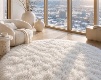 May include: A large, circular, off-white area rug featuring a thick, shaggy, and curly pile texture. The rug is positioned on a light-coloured wooden floor, showcasing a dense, soft, and fibrous surface that covers a significant portion of the room.