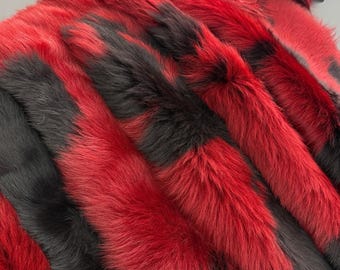 May include: A piece of smooth red leather folded at the top, layered over a thick, long-haired fur material featuring alternating vertical stripes of vibrant red and deep black. The fur has a dense, textured appearance with visible individual strands.