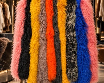 May include: A collection of long, shaggy, curly-textured faux fur scarves hanging side-by-side on a metal rack. The scarves feature a vibrant colour palette including pink, black, yellow, taupe, orange, dark grey, and bright blue.