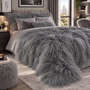 May include: A gray bed set featuring a long-pile faux fur comforter and matching shaggy pillows. The bedding includes a large, textured gray throw blanket draped over the bed, paired with smooth gray pillowcases and a small, fuzzy bolster pillow.