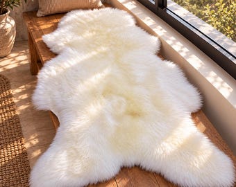 May include: A plush, off-white faux sheepskin rug with a long, dense pile and an irregular, organic shape. The rug features a soft, fluffy texture and a creamy, light-coloured appearance, designed to provide a thick, cushioned layer.