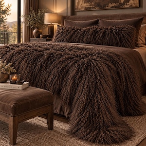 May include: A dark brown, long-pile, shaggy textured throw blanket draped over a bed, accompanied by a matching long, cylindrical bolster pillow. The bedding set features a deep, monochromatic brown color palette with a dense, curly fiber finish.