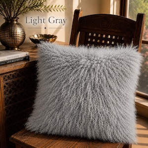 May include: A square throw pillow in a light gray color featuring a long, curly, shaggy texture across the entire surface. The pillow is positioned on a wooden chair. The text Light Gray is visible in the upper portion of the image.