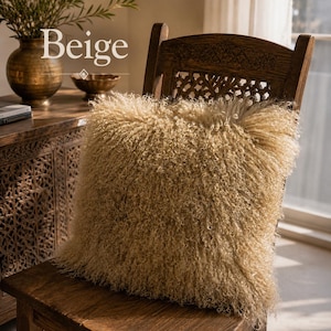 May include: A square beige throw pillow with a long, curly, shaggy texture resting on a wooden chair. The word Beige is printed in white text above the pillow. The pillow features a dense, high-pile surface with a consistent light tan color.