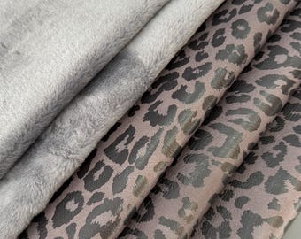 May include: A stack of folded fabric pieces featuring a solid light grey plush material on top, followed by two layers of a taupe-coloured material with a dark brown leopard print pattern. The textures appear soft and smooth with visible folds.
