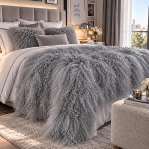May include: A gray shaggy faux fur bedspread with long, curly fibers draped over a bed. The bedding set includes two matching shaggy square pillows and a rectangular gray velvet pillow, all arranged on a white bed sheet with a gray border.
