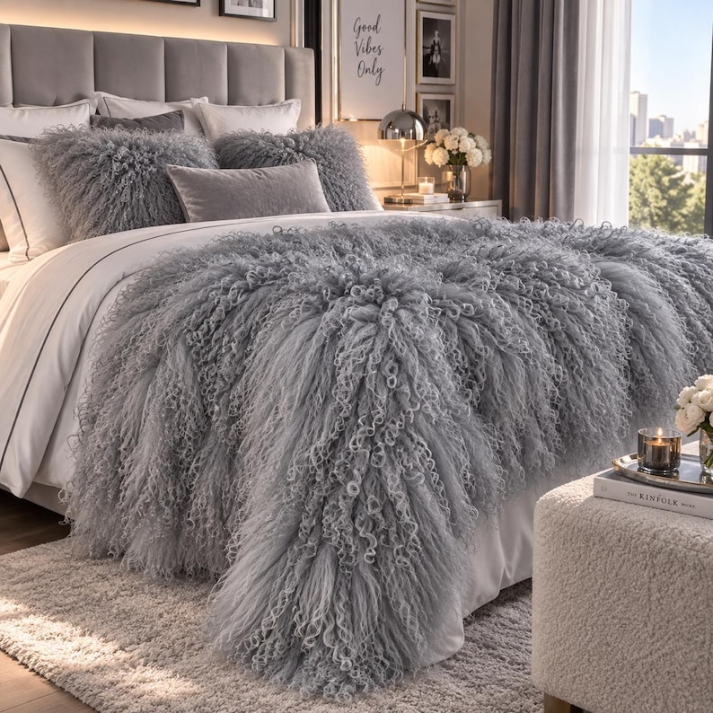 May include: A gray shaggy faux fur bedspread with long, curly fibers draped over a bed. The bedding set includes two matching shaggy square pillows and a rectangular gray velvet pillow, all arranged on a white bed sheet with a gray border.