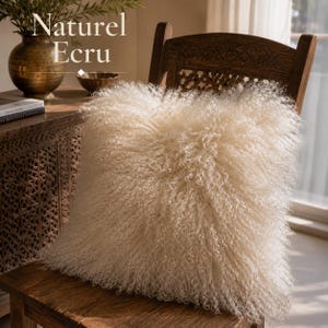 May include: A square ecru-colored throw pillow featuring long, curly, shaggy fibers on its surface. The pillow is positioned on a wooden chair. The text 'Naturel Ecru' is visible in the upper left corner of the image, set against a neutral background.