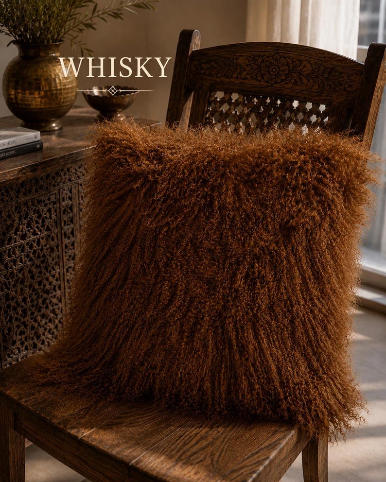 May include: A square throw pillow with long, curly, rust-brown fur texture resting on a dark wooden chair. The word WHISKY is printed in white capital letters above the pillow, accompanied by a small decorative diamond-shaped graphic element.