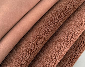 May include: A folded piece of fabric featuring two distinct textures. The top layer is a smooth, matte, light brown material, while the bottom layers consist of a thick, textured, dark brown faux shearling with a dense, curly pile surface.