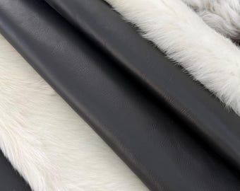 May include: A collection of layered materials featuring smooth black leather-like sheets alternating with strips of white faux fur. The textures contrast between the matte, grained surface of the black material and the soft, dense white fibres.