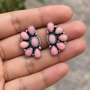 May include: A pair of stud earrings featuring multiple teardrop-shaped pink stones set in silver metal. Each earring is composed of several small, smooth, light pink cabochons arranged in a cluster, held by serrated silver bezels and small silver beads.