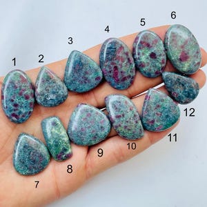 Puede incluir: Una colección de doce piedras preciosas pulidas, cada una con una forma única. Las piedras muestran una mezcla de tonos turquesa y verde, con inclusiones rojas vibrantes. Las piedras preciosas se sostienen en una mano, mostrando su belleza natural y variaciones.