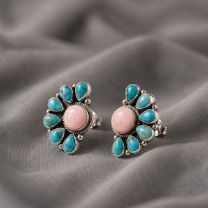 May include: A pair of stud earrings featuring a central round pink stone surrounded by a halo of seven teardrop-shaped turquoise stones set in silver. The design includes a twisted rope metal border around the center stone and small silver beads.