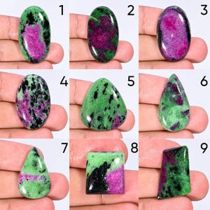 May include: A collection of nine polished ruby zoisite gemstones in various shapes, including oval, pear, and rectangular cuts. Each stone features a distinct pattern of vibrant magenta-pink ruby inclusions contrasted against green zoisite and black hornblende.