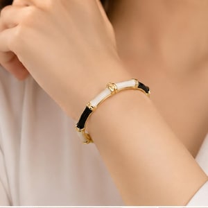 May include: A hinged bangle bracelet featuring a bamboo-inspired design with alternating segments of glossy black and white enamel. The structure is accented with polished gold-tone metal joints and trim, creating a sleek, segmented appearance.