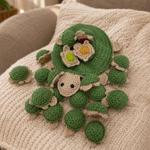 May include: A large green crocheted turtle with a tan head and black eyes, featuring a shell adorned with several smaller crocheted turtles in green, yellow, and white. The main turtle has a textured, rounded body and multiple small appendages.