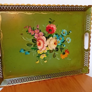 Op de afbeelding: Een rechthoekig olijfgroen metalen dienblad met een centraal bloemenboeket van roze, rode, gele en blauwe bloemen. Het dienblad heeft een geschulpte goudkleurige rand met een decoratief rasterpatroon en twee geïntegreerde handgrepen aan de zijkanten.