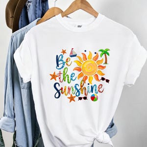 T-shirt graphique « Be The Sunshine » patchwork avec lettres, motif soleil et palmier, gris chiné, coupe oversize, style vacances positives et décontractées.