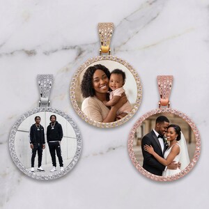 May include: Three round pendants with photos, each surrounded by a ring of small, clear stones. One pendant is gold-toned with a photo of a woman and baby. Another is silver-toned with two men. The third is rose gold with a couple.