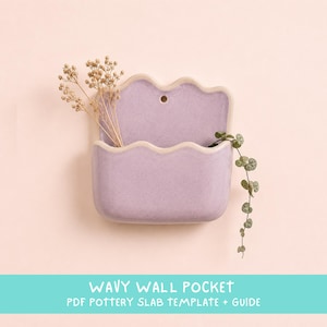 Könnte beinhalten: Eine lavendelfarbene Wandtasche aus Keramik mit gewelltem oberen Rand und einem kleinen runden Loch zur Befestigung. Die Tasche enthält getrocknete beige Blumen und eine grüne Ranke. Der Text WAVY WALL POCKET PDF POTTERY SLAB TEMPLATE + GUIDE ist sichtbar.