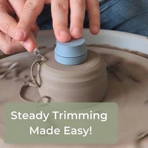 Puede incluir: Una herramienta de corte de cerámica azul claro está centrada en un torno de alfarero. La herramienta se utiliza para recortar una pieza de cerámica beige. El texto "Steady Trimming Made Easy!" se muestra en un rectángulo verde en la parte inferior de la imagen.