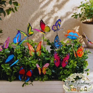 Può includere: Una collezione di farfalle colorate da giardino. Le farfalle hanno vari modelli e colori sulle ali, tra cui rosso, blu, giallo e rosa. Sono posizionate tra il fogliame verde in una fioriera bianca, creando una vivace decorazione esterna.