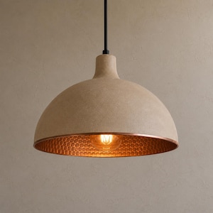 Peut inclure: Une suspension en forme de dôme avec un extérieur beige texturé et un intérieur en cuivre métallique présentant un motif en nid d'abeille. Le luminaire est suspendu par une fine tige noire et contient une ampoule de style Edison.